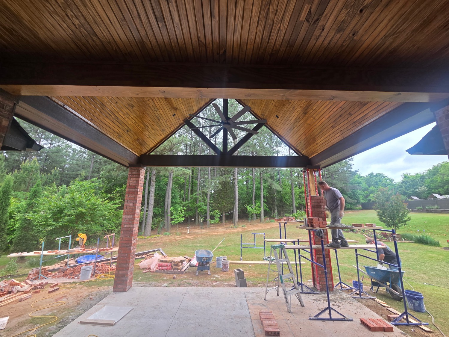 Mason laying a brick column under a wood porch ceiling
